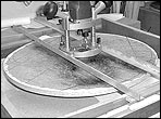 A router assembly rides on curved side rails to cut a dished workboard.